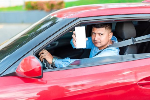 Handsome driver showing cell phone screen outdoors. Smiling male driver showing cell phone screen