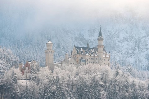 Snow-covered castle in a winter forest, surrounded by misty mountains and frosty weather,