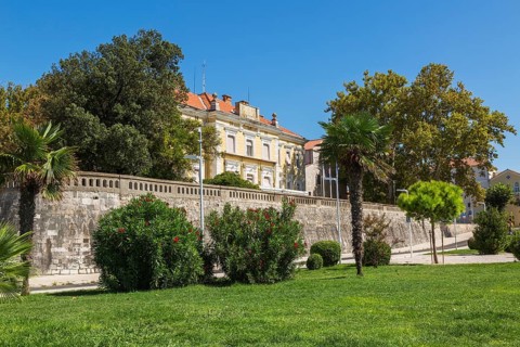 Landscaped park with green grass lawn and old yellow architectural building with terracotta clay