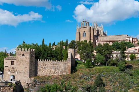 Medieval cityscape with church, city walls and trees under a blue sky with clouds, Puente de San