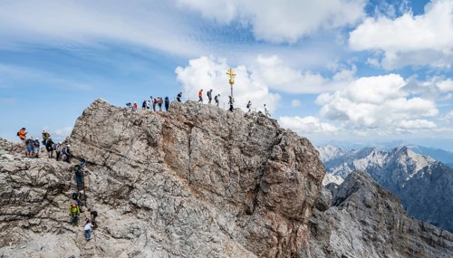 Tourists queue up for the summit of the Zugspitze, summit with golden summit cross, overtourism,