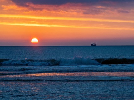 Silhouette of a fishing boat against a colorful sunset over the North Sea, and waves breaking on