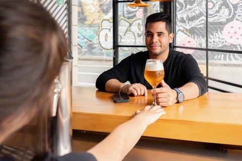 A man smiles as he receives a freshly poured beer from a bartender at the bar of a contemporary bar
