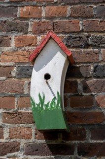 A colourful birdhouse with a plant motif on a brick wall in the sunlight, Münsterland, North