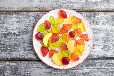 Various fruit jelly candies on plate on gray wooden background. top view, flat lay, close up