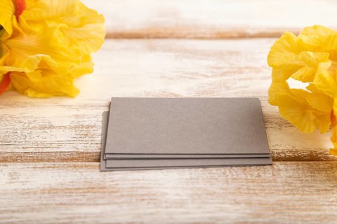 Gray business card with iris yellow flowers on white wooden background. side view, copy space,
