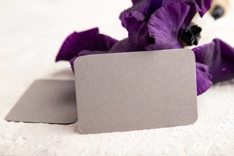 Gray business card with violet iris flowers on white concrete background. side view, copy space,