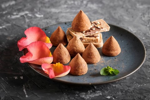 Chocolate truffle on blue ceramic plate decorated with rose petals on black concrete background.