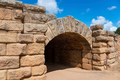 Historic stone archway from Roman times, surrounded by thick stone walls under a blue sky, Mérida,