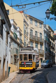 Yellow tram runs through narrow streets with historic buildings under a blue sky, Tram, Line 28,