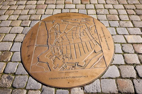 Fountain of the Materni Hospital, bronze fountain slab, cobblestone pavement, street An der