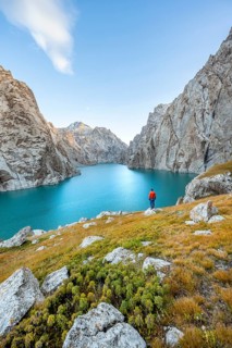 Young man at the turquoise mountain lake Kol Suu with rocky steep mountains, Kol Suu Lake, Sary