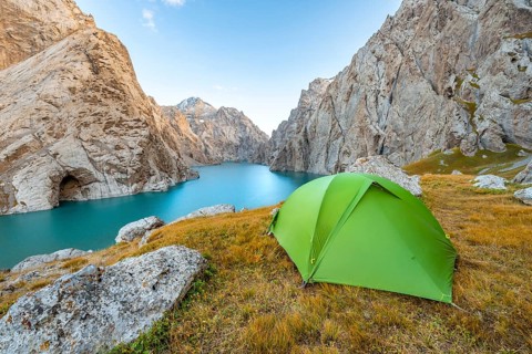 Green tent at the turquoise mountain lake Kol Suu with rocky steep mountains, Kol Suu Lake, Sary