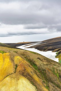 Two hikers on a hill in the distance, colourful volcanic landscape with hills and snow, Laugavegur