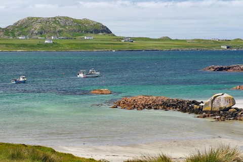 Some boats on the sea in front of a rocky coast, island with houses, view of Iona, Port of