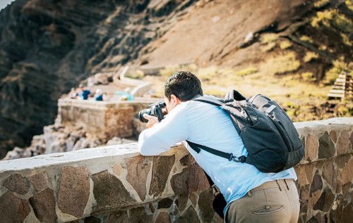 A tourist man with a photo camera taking photos at a viewpoint. Adventurous man with his camera