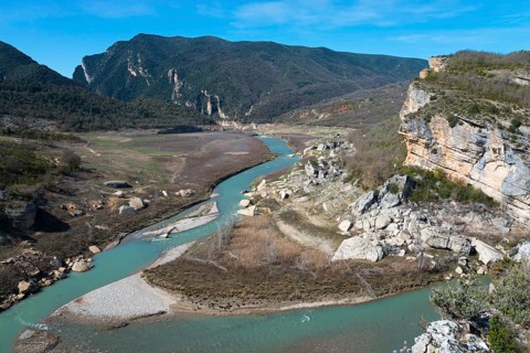 A winding river cuts through rocky landscapes and green hills, surrounded by steep mountains under