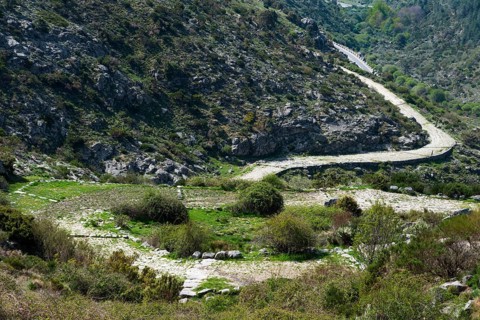 A winding path runs through a hilly and green landscape with rocky elevations, old Roman road, at