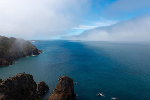 Steep cliffs jut into the blue sea under a cloudy sky, fog, Cape Cabo da Roca, westernmost point of