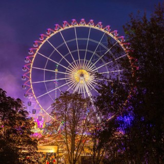 A large, brightly lit Ferris wheel with colourful lights against a night sky and surrounded by