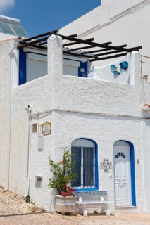 White and blue Mediterranean house with flowers in front of a terrace under a clear sky, Albufeira,