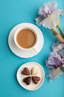 Cup of cioffee with chocolate candies and lilac iris flowers on blue pastel background. top view,