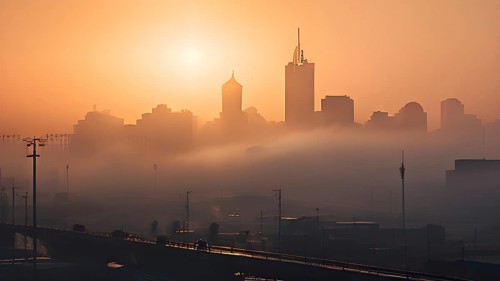 Cityscape emerging from a dense enveloping fog in sunrise and skyscrapers piercing the haze, AI
