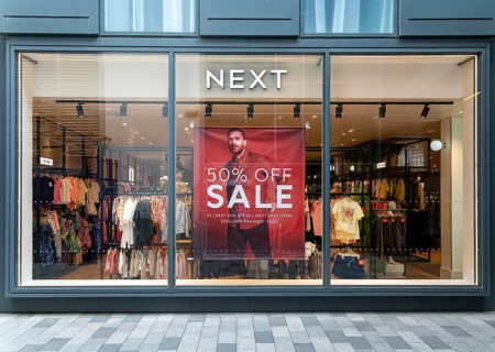 Poster advertising 50% off sale in shop window of Next sture, Newbury, Berkshire, England, UK