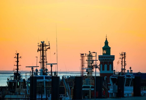 Harbour at sunset with various boats and the sea in the background, the sky in bright orange,