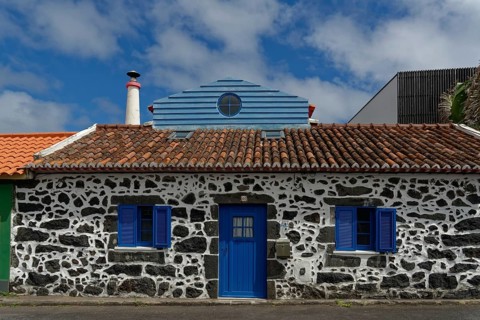 Former whaler's stone house with blue shutters and door, traditional tiled roof, narrow chimney,