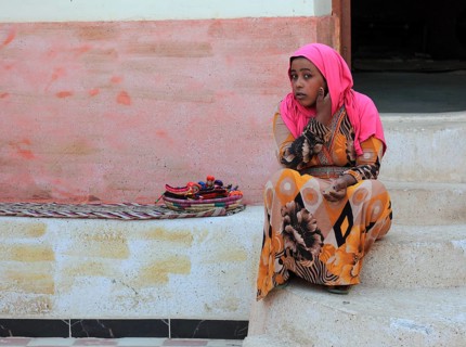 In a Nubian village, young girl with headscarf sitting on the ground, Egypt, Africa