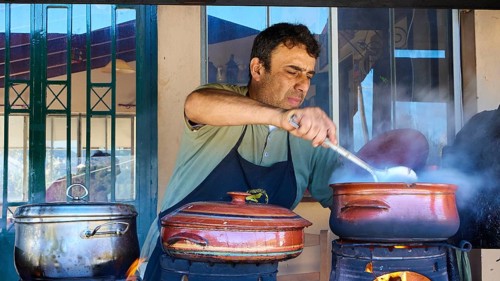 Chef Stelios, A man stirs in a pot on an open fire in a rustic kitchen while other pots stand next