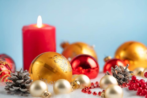 Burning candle with red and gold baubles and pine cones on artificial snow, festive atmosphere
