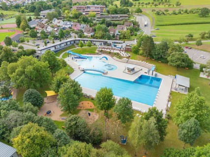 Aerial view of an outdoor swimming pool with several pools, slides and surrounding trees in a green