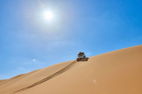 Off-road vehicle drives over a sand dune under a bright blue sky in the desert, Matruh, Great Sand
