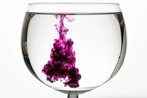 Purple swirls of colour unfold in a glass of water, creating a creative and abstract atmosphere