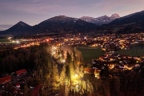 Illuminated town at dusk, surrounded by mountains and forests, creates a cosy atmosphere,