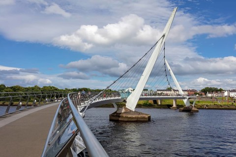 An impressive bridge arch stretching over a river under a cloudy sky, Londonderry