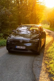 Car driving on a sunlit forest path, warm rays of light illuminate the road, electric car, VW ID5,