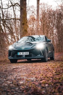 Black car on a forest path with shining headlights in an autumnal ambience, e-car sharing vehicle