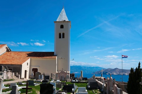 Church tower and gravestones with a view of the sea and mountains, Croatian flag, peaceful