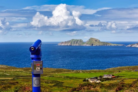 Viewpoint with blue telescope, coin-operated telescope on the coast, rocky islands on the horizon,