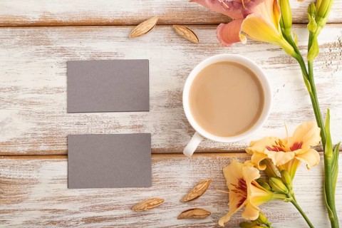 Gray paper business card mockup with orange day-lily flower and cup of coffee on white wooden