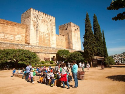 Children on a school trip sitting outside the fortified castle walls of the historic Alcazaba, of