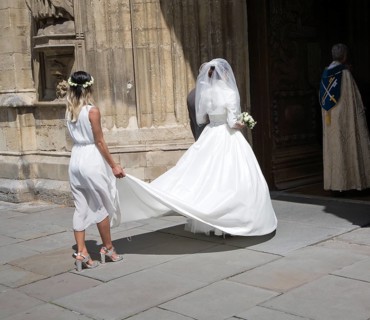Bride wearing white wedding dress with her bridesmaid as they enter Bath Abbey church, Bath,
