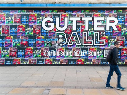 Person waking past posters on shopfront advertising Gutter Ball ten pin bowling attraction,