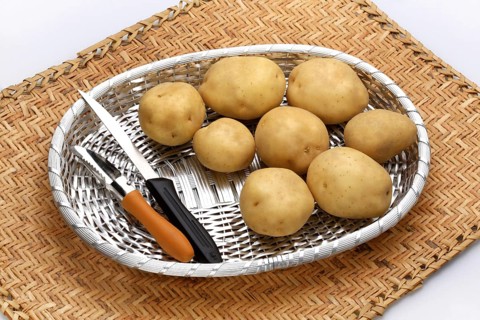 Potatoes Latin Solamum Tuberosum in silver basket with knife and peeler used as vegetables and