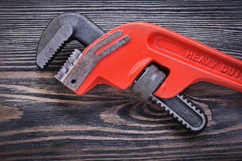 Adjustable monkey wrench on wooden board directly above plumbing concept