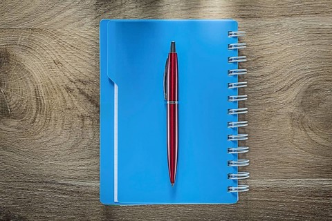 Biro pen spiral copybook on wooden board