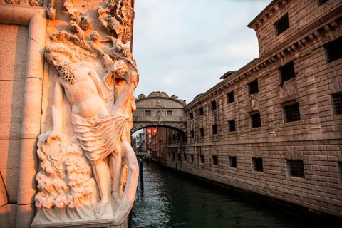 Morning light falls on a stone sculpture of an ancient deity, behind the Bridge of Sighs or Ponte